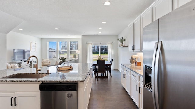 kitchen with open floor plan, dark wood-type flooring, white cabinetry, a sink, and stainless steel appliances