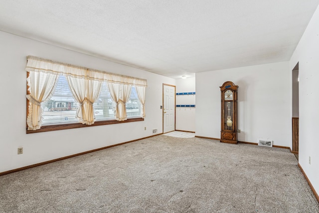 empty room with a textured ceiling, baseboards, visible vents, and carpet floors