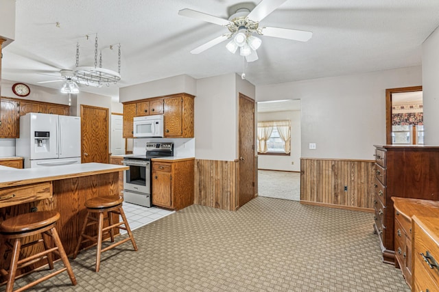 kitchen featuring white appliances, wooden walls, a ceiling fan, and a wainscoted wall