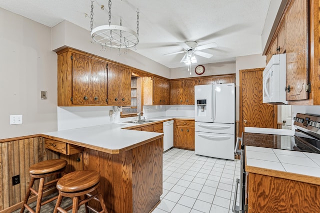kitchen with white appliances, brown cabinetry, a peninsula, and ceiling fan