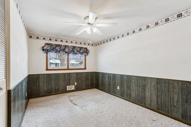 carpeted empty room with a ceiling fan, a textured ceiling, wood walls, and wainscoting