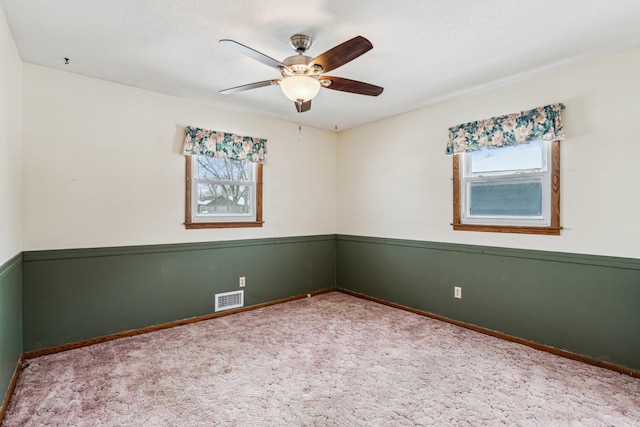carpeted spare room featuring a wealth of natural light, visible vents, and a ceiling fan