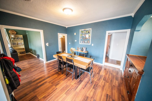 dining area with arched walkways, ornamental molding, wood finished floors, and a textured ceiling
