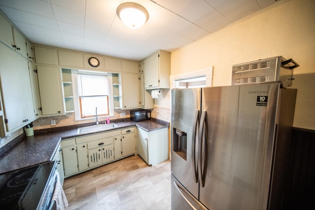 kitchen with dark countertops, open shelves, a sink, cream cabinets, and stainless steel appliances