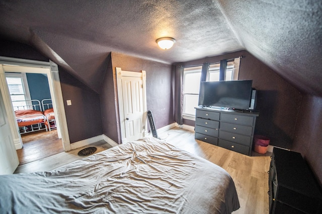 bedroom with vaulted ceiling, baseboards, a textured ceiling, and light wood-style floors