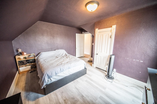 bedroom with vaulted ceiling, wood finished floors, baseboards, and a textured wall