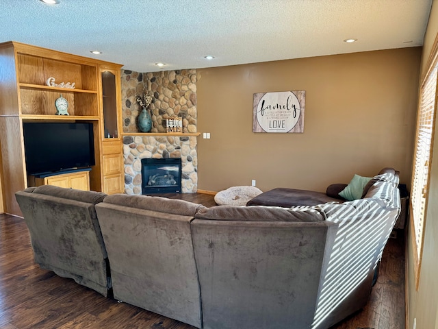 living room with dark wood-style floors, recessed lighting, a textured ceiling, and a stone fireplace