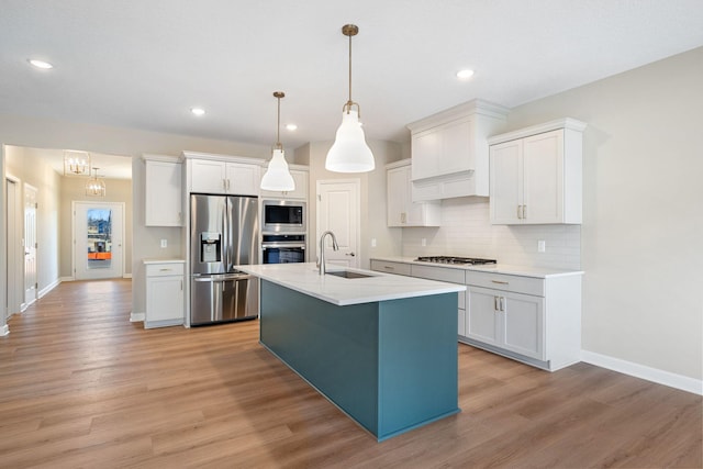 kitchen with light countertops, a sink, light wood finished floors, stainless steel appliances, and decorative backsplash