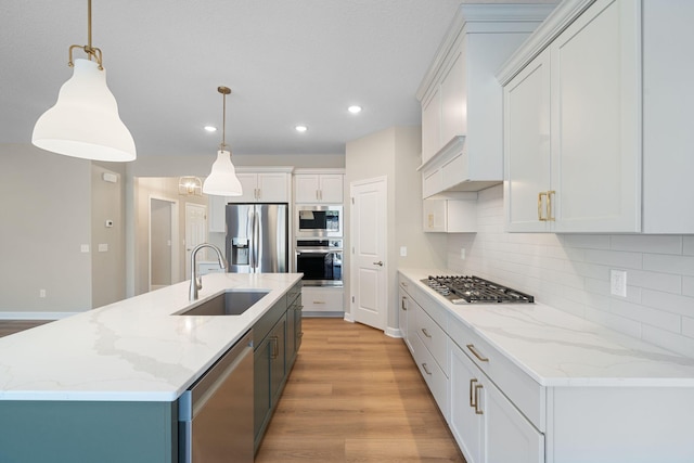 kitchen featuring stainless steel appliances, backsplash, a center island with sink, a sink, and light wood-style floors