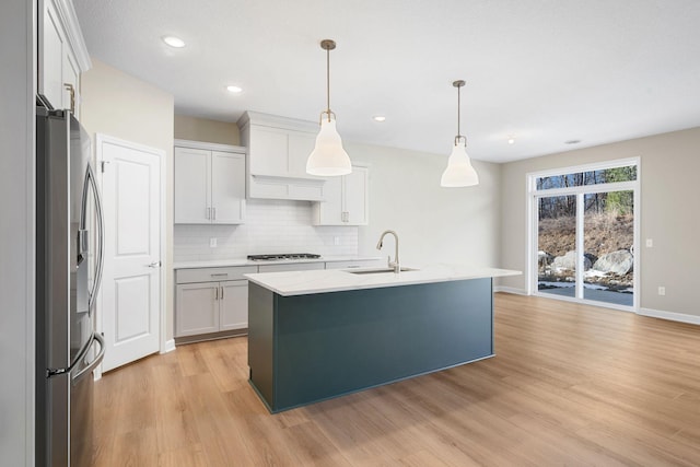 kitchen with stainless steel appliances, backsplash, a sink, light wood-style floors, and pendant lighting