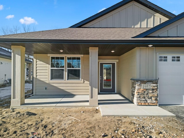 doorway to property with central AC unit, a garage, board and batten siding, roof with shingles, and covered porch