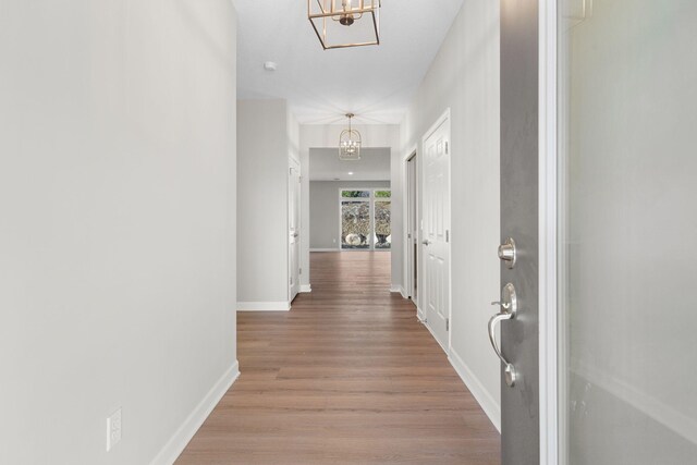 hall with an inviting chandelier, baseboards, and light wood-style floors