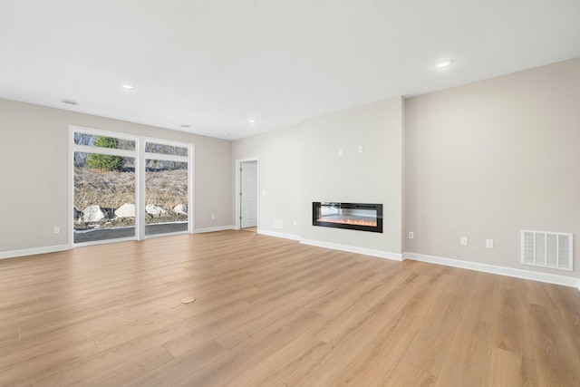 unfurnished living room with baseboards, visible vents, a glass covered fireplace, and light wood-style floors