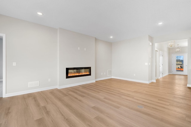 unfurnished living room featuring visible vents, a notable chandelier, light wood-style floors, and a glass covered fireplace