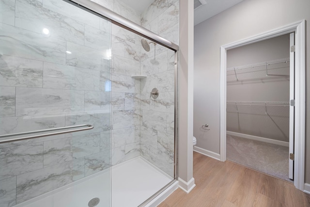 bathroom featuring baseboards, wood finished floors, toilet, a stall shower, and a walk in closet