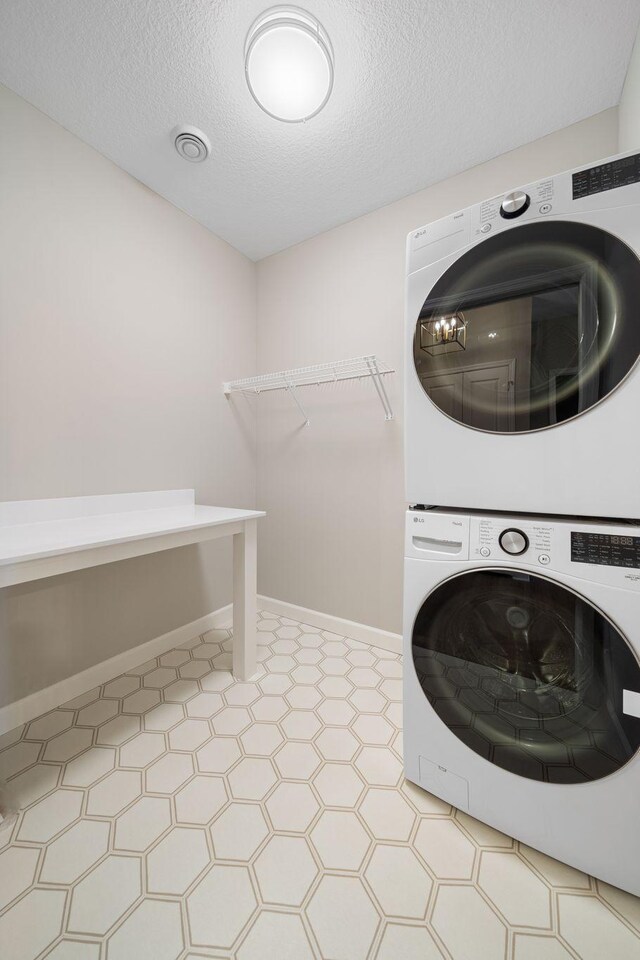 clothes washing area featuring baseboards, a textured ceiling, stacked washer / dryer, and laundry area