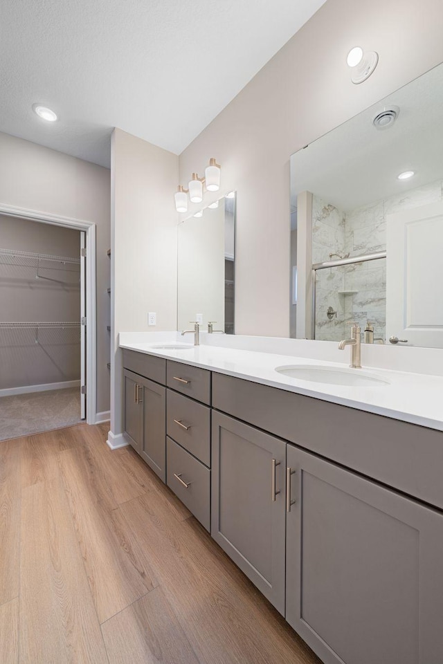 bathroom with a walk in closet, a shower stall, a sink, double vanity, and wood finished floors