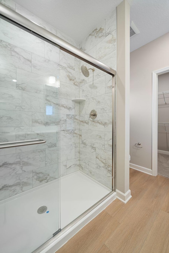 bathroom with toilet, a shower stall, wood finished floors, a walk in closet, and baseboards