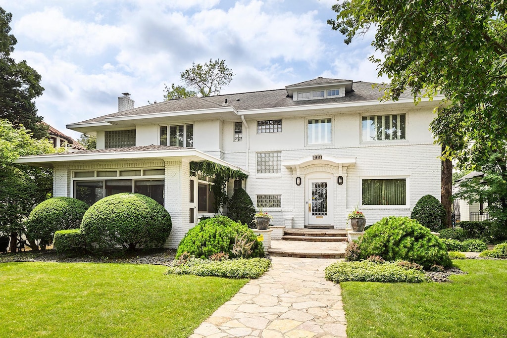 view of front of property featuring brick siding, a chimney, a sunroom, and a front yard