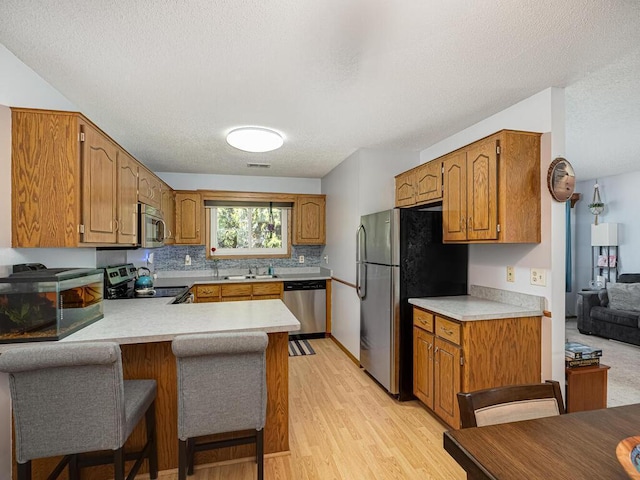 4237 Centerville Rd, Vadnais Heights, MN 55127 - kitchen featuring stainless steel appliances, a peninsula, light countertops, brown cabinetry, and a textured ceiling