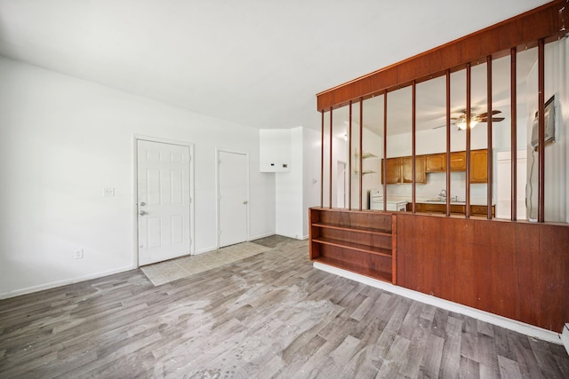 unfurnished living room with wood finished floors, baseboards, a sink, and washer / clothes dryer