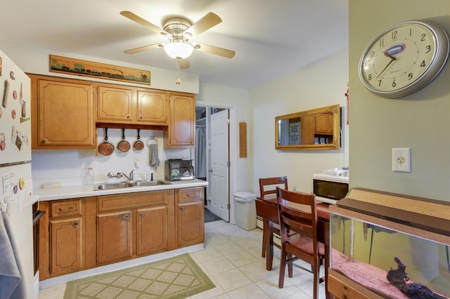 kitchen with light countertops, a ceiling fan, a sink, freestanding refrigerator, and brown cabinetry
