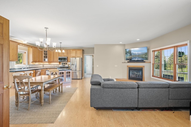 living area with a glass covered fireplace, recessed lighting, an inviting chandelier, and light wood-type flooring