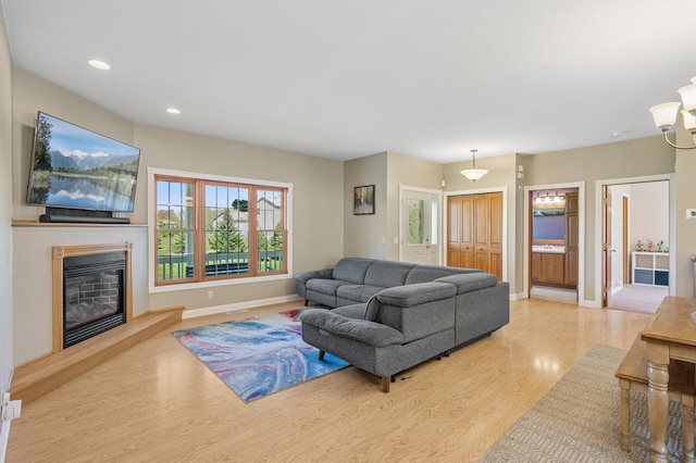 living area featuring wood finished floors, baseboards, a glass covered fireplace, a chandelier, and recessed lighting