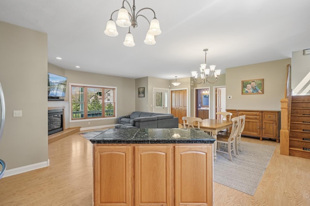 kitchen featuring light wood-type flooring, pendant lighting, an inviting chandelier, a kitchen island, and a glass covered fireplace