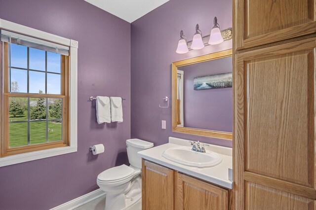 half bath with baseboards, vanity, and toilet