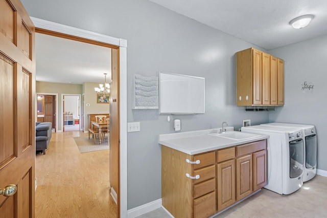 laundry area with a sink, cabinet space, separate washer and dryer, an inviting chandelier, and baseboards