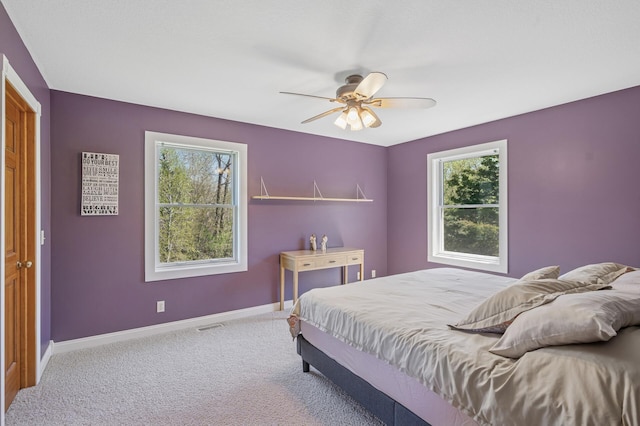 carpeted bedroom with baseboards, multiple windows, visible vents, and ceiling fan