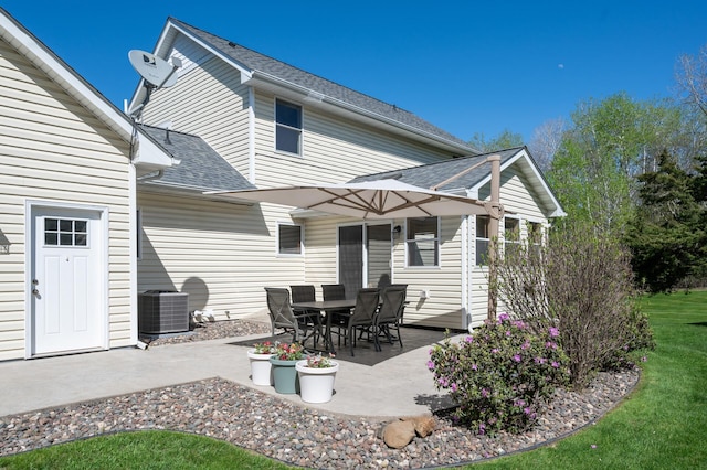 rear view of property with cooling unit, a patio area, roof with shingles, and a lawn