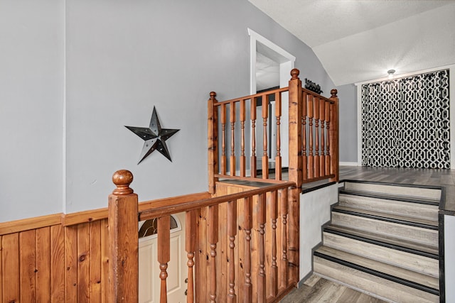 stairway featuring wood finished floors, a textured ceiling, and vaulted ceiling