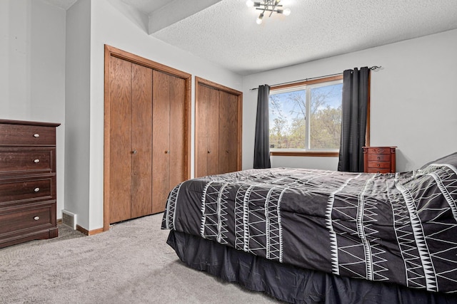 bedroom featuring a textured ceiling, baseboards, carpet flooring, visible vents, and two closets