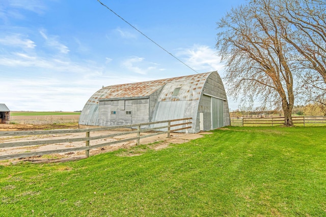 view of barn featuring a rural view, a yard, and fence