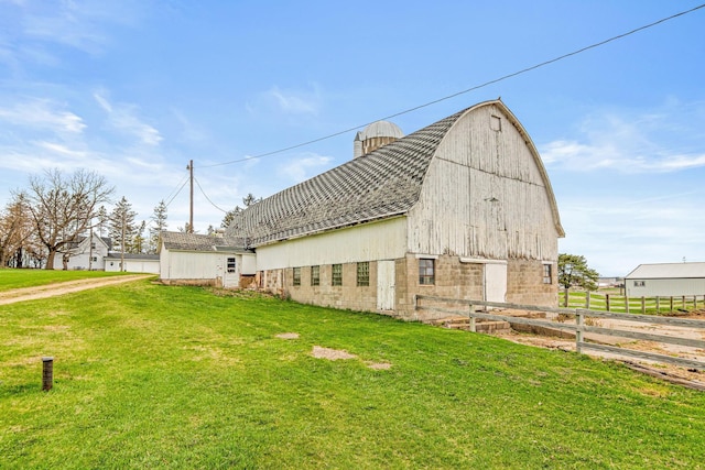 exterior space featuring fence, an outdoor structure, a gambrel roof, a barn, and a lawn
