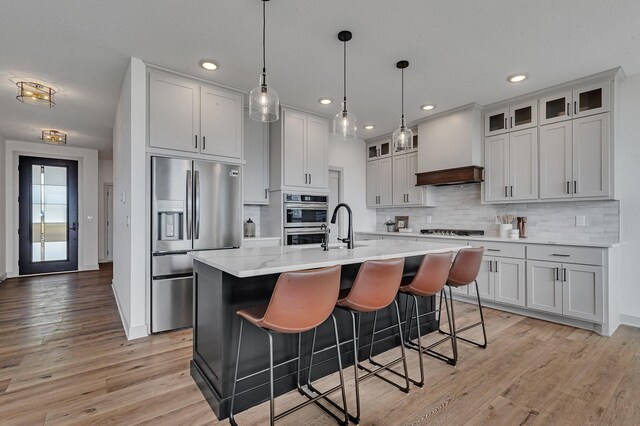 kitchen featuring stainless steel appliances, backsplash, light wood-style floors, recessed lighting, and a kitchen island with sink