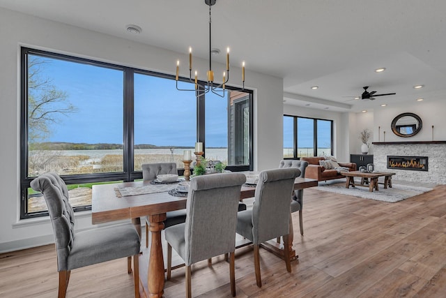 dining room featuring wood finished floors, a water view, a stone fireplace, recessed lighting, and a chandelier