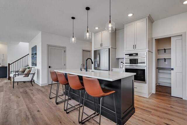 kitchen featuring appliances with stainless steel finishes, light wood finished floors, a center island with sink, a sink, and a kitchen breakfast bar
