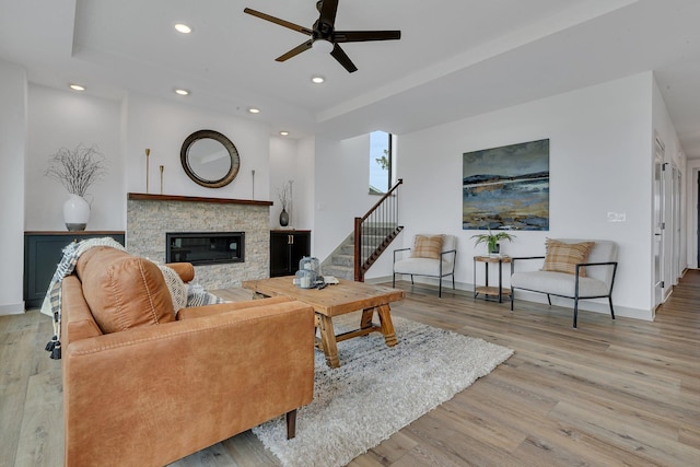 living area featuring a ceiling fan, wood finished floors, a stone fireplace, a raised ceiling, and recessed lighting
