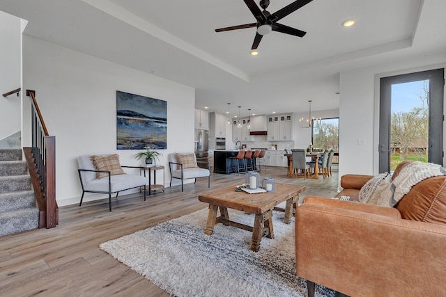 living area with light wood finished floors, a ceiling fan, stairway, a tray ceiling, and recessed lighting