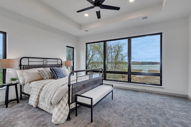 carpeted bedroom with recessed lighting, baseboards, a water view, a tray ceiling, and a ceiling fan