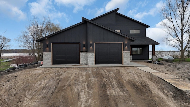 view of front of home with dirt driveway, stone siding, a garage, and board and batten siding