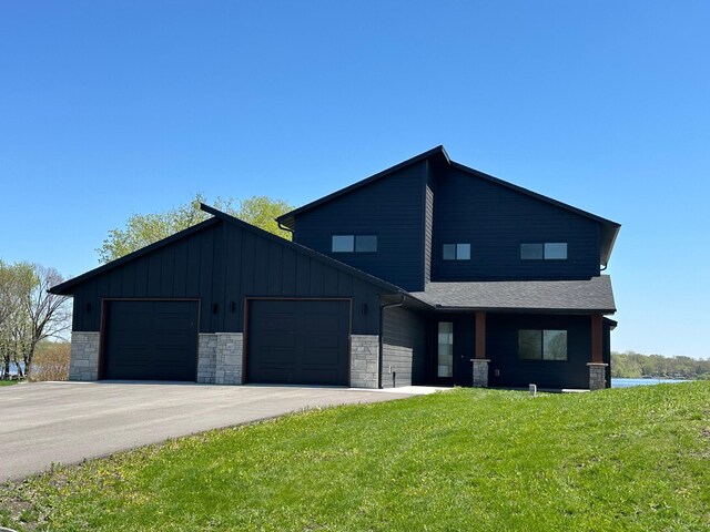 view of front of property featuring stone siding, a garage, a front yard, board and batten siding, and driveway