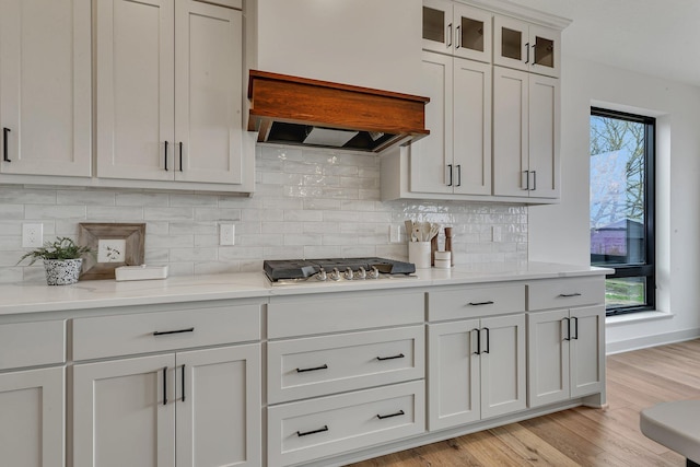 21070 Eagle Dr, Osakis, MN 56360 - kitchen featuring stainless steel gas cooktop, light wood finished floors, decorative backsplash, glass insert cabinets, and white cabinetry