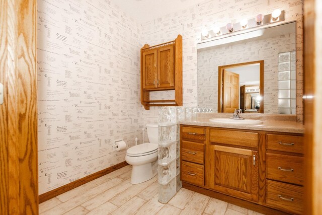 15671 Wermager Beach Rd, Lake Park, MN 56554 - bathroom featuring wallpapered walls, vanity, toilet, wood finished floors, and baseboards