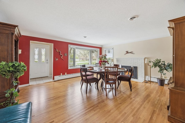 5427 Twin Lake Blvd E, Brooklyn Center, MN 55429 - dining room with baseboard heating, light wood-type flooring, healthy amount of natural light, a textured ceiling, and a brick fireplace