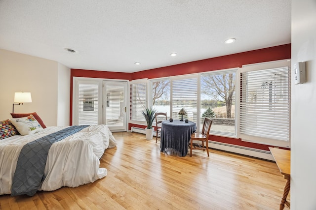 5427 Twin Lake Blvd E, Brooklyn Center, MN 55429 - bedroom featuring a baseboard heating unit, light wood-style floors, a textured ceiling, access to outside, and baseboard heating