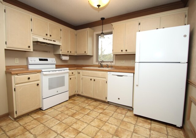 kitchen with stone finish flooring, a sink, light countertops, under cabinet range hood, and white appliances